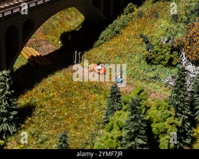 Un homme marche sur un chemin dans un champ avec un train jouet. Le train est sur une voie qui se trouve sous un pont Banque D'Images