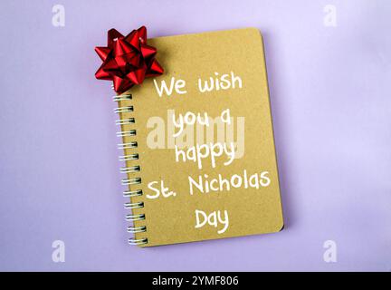 Cahier avec un arc rouge sur le dessus et les mots We Wish You a Happy compris Nicholas Day écrit dessus Banque D'Images