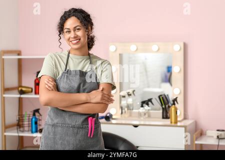 Beau jeune heureux coiffeur afro-américain avec des pinces à cheveux dans le salon de beauté Banque D'Images