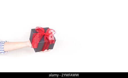 Un élégant coffret cadeau noir orné d'un ruban rouge vif et d'un noeud, isolé sur un fond blanc, parfait pour diverses occasions et idéal pour les marchés Banque D'Images