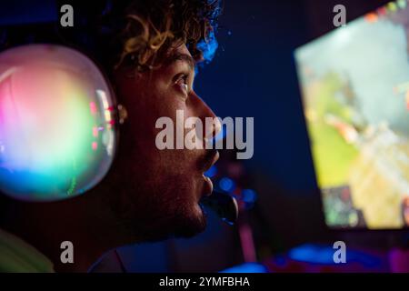 Photo de jeune homme mignon excité émerveillé jouer joueur ordinateur violet bleu néon lumière à l'intérieur tard dans la nuit Banque D'Images