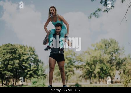 Amis joyeux s'engageant dans des activités d'entraînement ludiques dans un parc par une journée ensoleillée, mettant en valeur le travail d'équipe, la force et l'enthousiasme. Banque D'Images