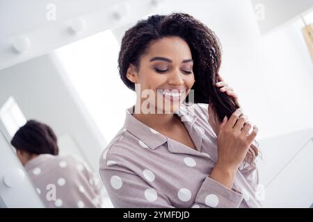 Jeune femme aux cheveux afro souriant paisiblement en vêtements de nuit, profitant d'un moment matinal à la maison, à l'intérieur Banque D'Images