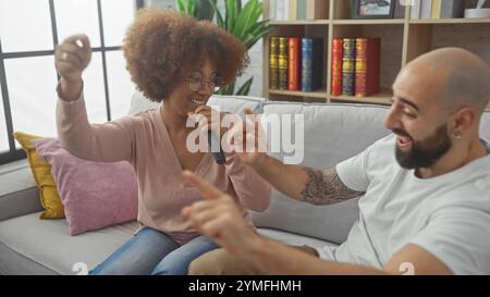 Un joyeux couple interracial profiter de chanter avec une télécommande comme un microphone dans un cadre de salon confortable. Banque D'Images