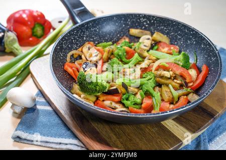 Légumes mélangés colorés dans une poêle à frire tels que brocoli, poivrons, champignons, aubergines et oignons sur une planche de cuisine en bois, végétarien en bonne santé Banque D'Images