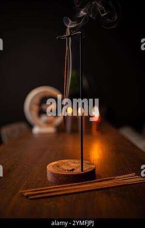 Un bâton d'encens brûlant et générant de la fumée aromatique entouré de petites bougies Banque D'Images