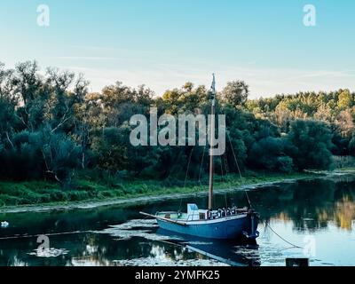 Un petit bateau flotte sur une rivière avec des arbres en arrière-plan. Le bateau est la seule chose visible dans l'eau, et il se déplace lentement. La scène Banque D'Images