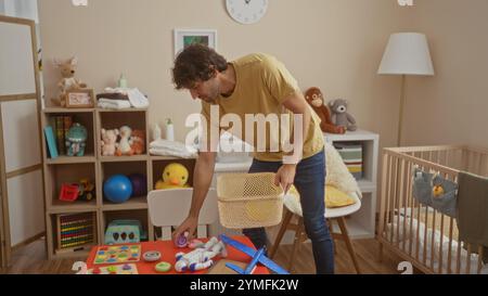 Jeune homme organisant des jouets et des articles pour bébé dans une chambre confortable, avec un berceau, un décor coloré et une atmosphère accueillante capturant l'essence de nourrir c Banque D'Images