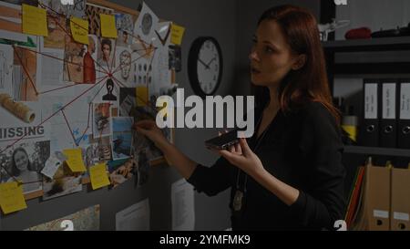 Une jeune femme détective aux cheveux roux analyse les preuves dans un bureau sombre, entourée de dossiers et d'un mur d'indices. Banque D'Images