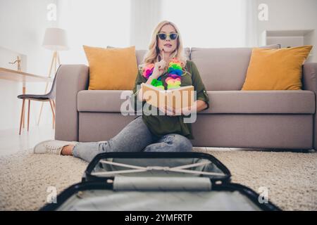 Photo de charmante femme assise sur le sol écrivant des plans pour un futur voyage de week-end organisant une valise à l'intérieur d'un appartement plat Banque D'Images