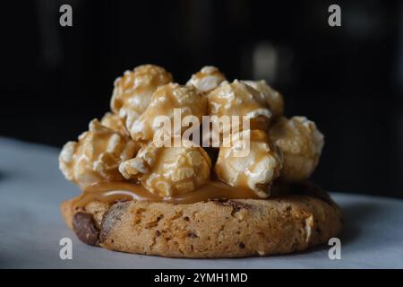 Gros plan sur un biscuit aux pépites de chocolat traditionnel américain fait maison avec garniture de pop-corn au caramel. Sur fond noir. Banque D'Images