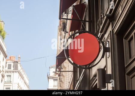 Panneau de magasin de cercle rouge vide sur une rue européenne, suspendu sur un mur sous des auvents décoratifs, soulignant le design minimaliste et la devanture urbaine aes Banque D'Images