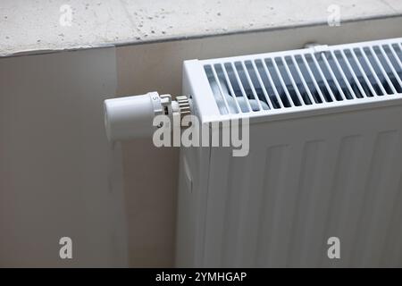 Radiateur blanc moderne avec vanne thermostatique réglable installée près du rebord de la fenêtre dans une pièce lumineuse pendant les travaux de rénovation. Banque D'Images