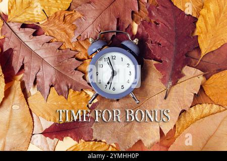 Horloge est au-dessus d'une pile de feuilles avec les mots Time for Bonus écrit en dessous Banque D'Images