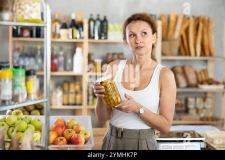 Femme shopper choisissant soigneusement le pot d'olives en conserve dans le supermarché d'épicerie Banque D'Images