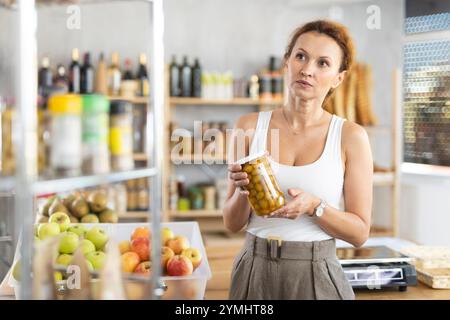 Femme shopper choisissant soigneusement le pot d'olives en conserve dans le supermarché d'épicerie Banque D'Images