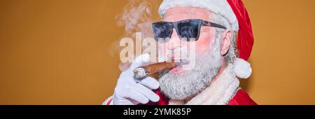 Père Noël portant des lunettes de soleil et fumant cigare sur un fond orange Banque D'Images