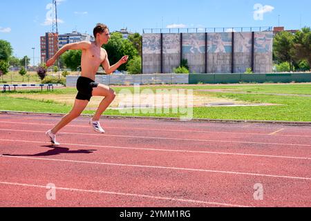 Un homme qui court sur une piste avec un bâtiment en arrière-plan. L'homme porte un short noir et pas de chemise Banque D'Images