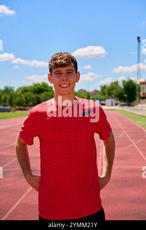 Un jeune homme en chemise rouge se tient sur une piste. Il sourit et pose pour une photo Banque D'Images