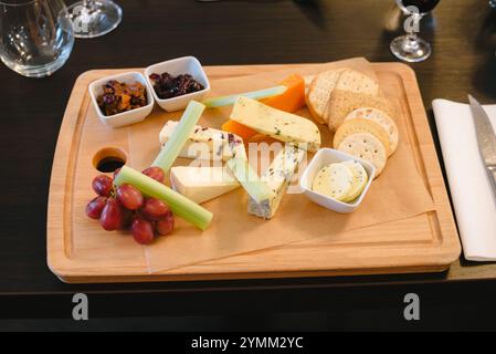 Une planche de bois avec une variété de fromages et de craquelins. La planche est placée sur une table avec un couteau et un verre à vin Banque D'Images