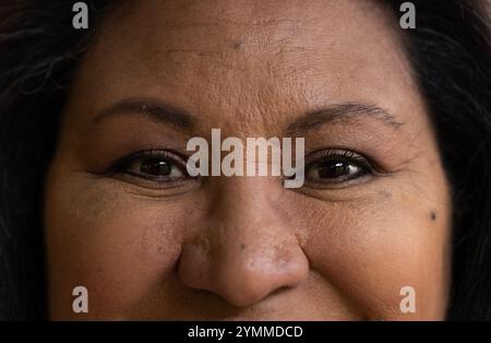 Femme âgée souriante avec des yeux chauds et heureux en vue rapprochée, exprimant la joie, à la maison. Bonheur, joyeux, positif, émotions, portrait, contentement Banque D'Images