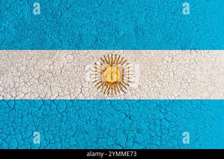 Lit de lac d'argile fissuré avec drapeau argentin peint dessus (gros plan). Concept de changement climatique, sécheresse et assèchement de l'eau en Argentine Banque D'Images
