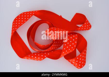 Des rubans de satin rouge vif avec des pois blancs sont situés sur un fond en plastique blanc. Banque D'Images