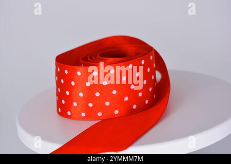 Des rubans de satin rouge vif avec des pois blancs sont situés sur un fond en plastique blanc. Banque D'Images