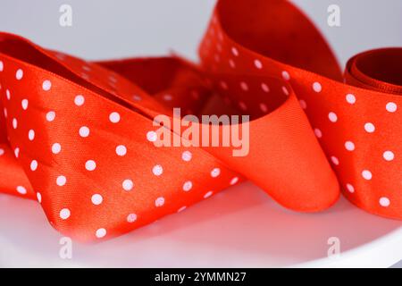 Des rubans de satin rouge vif avec des pois blancs sont situés sur un fond en plastique blanc. Banque D'Images