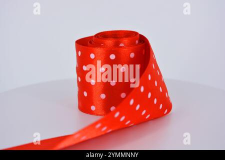 Des rubans de satin rouge vif avec des pois blancs sont situés sur un fond en plastique blanc. Banque D'Images