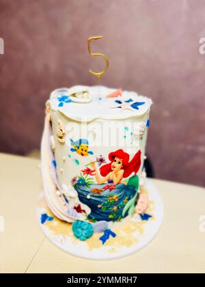 Kiev, Ukraine - 22 novembre 2024 : un gâteau d'anniversaire dynamique et fantaisiste sur le thème de la sirène Ariel orné de décorations de l'océan et d'un topper numéro cinq. Banque D'Images