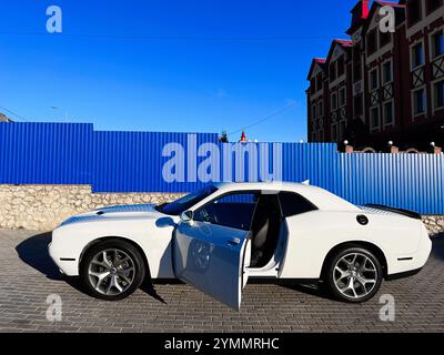 Kiev, Ukraine - 22 novembre 2024 : une voiture blanche moderne Dodge Challenger avec une porte ouverte est garée dans une rue de la ville, mettant en valeur l'architecture urbaine et Banque D'Images