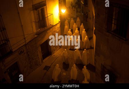 Des pénitents à capuche habillant des capes blanches traversent une rue fléchée lors d'une procession de la semaine Sainte de Pâques à Trujillo, en Estrémadure, en Espagne. Banque D'Images