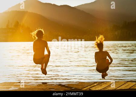 Deux jeunes femmes heureuses sautant dans un lac au coucher du soleil dans l'Idaho. Banque D'Images