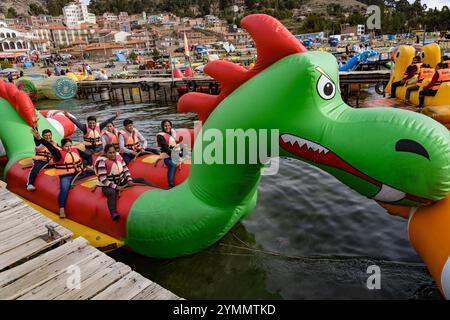 Touristes appréciant une balade sur un bateau dragon gonflable coloré sur le lac titicaca, avec la ville de puno en arrière-plan Banque D'Images