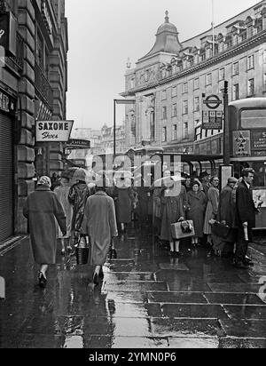 Les passagers attendent sous la pluie pour les bus pendant l'heure de pointe dans Regent Street de Londres, vers 1960 Banque D'Images