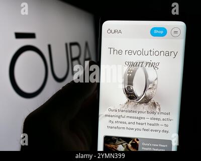 Dans cette illustration photo, une personne tient un téléphone portable avec la page Web de la société finlandaise de technologie de la santé Oura Health Oy devant le logo. Banque D'Images