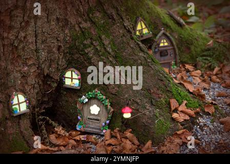 Une scène forestière fantaisiste mettant en scène un petit village de conte de fées sculpté dans les racines d'un grand arbre. Le village comprend des fenêtres lumineuses avec d floral Banque D'Images