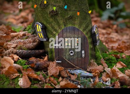 Une charmante porte de fée miniature avec de petites fenêtres et des lumières colorées, nichée à la base d'un arbre dans une forêt. La porte indique "Fairies Welcome" A. Banque D'Images