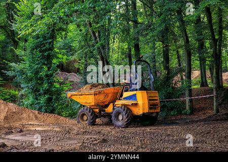 Un petit camion à benne basculante orange enlève la terre d'un chantier de construction dans un parc. Banque D'Images