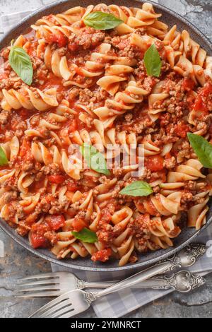 Pâtes bolognaises Fusilli avec sauce tomate, bœuf haché haché haché, feuilles de basilic en gros plan sur l'assiette sur la table. Vue de dessus verticale Banque D'Images
