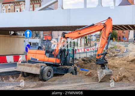 Une excavatrice orange se tient sur une section de route creusée en réparation sous un pont. Banque D'Images