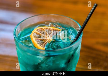 Un cocktail préparé avec du liqueur Blue Curaçao, la spécialité turquoise distinctive de Senior & Co., Landhuis Chobolobo, Schottegatweg Oost, Willemstad, Curaçao : servi avec des glaçons, une tranche d'orange séchée et une paille noire. La couleur bleue est obtenue en ajoutant du colorant alimentaire au distillat par ailleurs incolore fait à partir de pelures d'orange Laraha. Banque D'Images