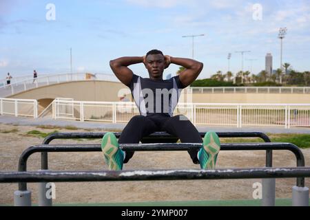 Athlète noir effectuant des sit-ups calisthéniques sur des barres parallèles à l'extérieur Banque D'Images
