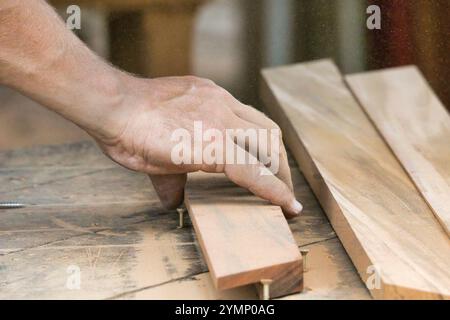 Un homme travaille sur un morceau de bois. Le bois est coupé et l'homme utilise une vis pour le maintenir en place. Concept d'artisanat et de dévouement Banque D'Images