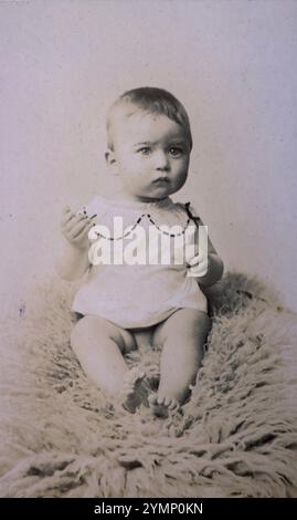 Sépia tone carte de visite studio photographie d'une petite fille dans une couche et une robe, assise sur un tapis. Du photographe français F. Rovelli du 11 Avenue de la Gare, Vesoul, France ; cette photo serait d'environ 1880.. Banque D'Images