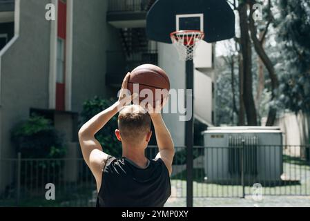 Vue arrière d'un joueur de streetball tirant un ballon de basket-ball. Jeune homme jouant au basket-ball sur un terrain extérieur un jour d'été. Photo de haute qualité Banque D'Images