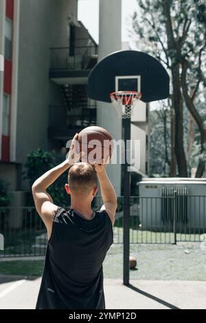 Vue arrière d'un joueur de streetball tirant un ballon de basket-ball. Jeune homme jouant au basket-ball sur un terrain extérieur un jour d'été. Photo de haute qualité Banque D'Images