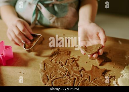 Mains coupant la pâte à pain d'épices sur la table, en utilisant des emporte-pièces en forme d'étoile, créant des formes festives. La pâte et la farine sont étalées sur la surface, avec quelques formes de biscuits déjà coupées et soulevées Banque D'Images