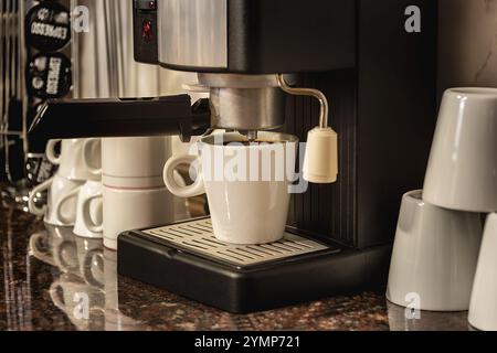 Machine à café avec une tasse, sur le comptoir de cuisine et fond flou. Banque D'Images